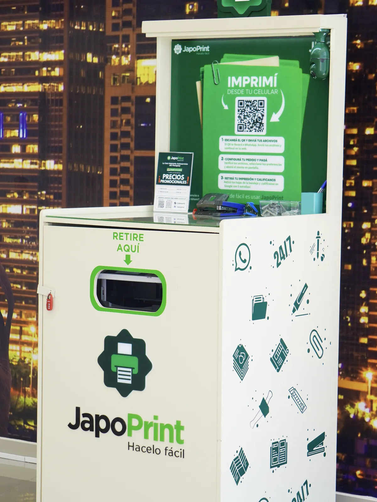 Tótem JapoPrint iluminado de noche, con la ciudad de fondo